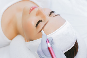 Beautiful young girl with long eyelashes tweezing her eyebrows in a beauty salon. Eyebrow Correction. Beauty Concept. Permanent Makeup. Microblading brow.  Beautician Doing brows Tattooing.