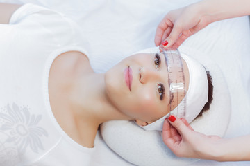 Beautiful young girl correction of eyebrows in a salon.professional care for face.Permanent Makeup for brows. woman tweezing her eyebrows in salon.Cosmetology Treatment.Make-Up.Microblading eyebrows.