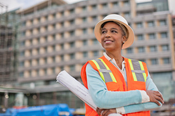 Proud young female engineer holding a roll of building plans on a construction site.