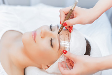 Beautiful young girl correction of eyebrows in a salon.professional care for face.Permanent Makeup for brows. woman tweezing her eyebrows in salon.Cosmetology Treatment.Make-Up.Microblading eyebrows.