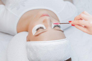 Obraz na płótnie Canvas Eyelash Extension Procedure. Close up view of beautiful Woman with Long Eyelashes. Stylist holding tweezers, tongs and making lengthening lashes for girl in a beauty salon. Beauty Concept.