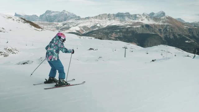 Following route of little girl on ski slopes heading downhill. Vast white mountain range in background view.
