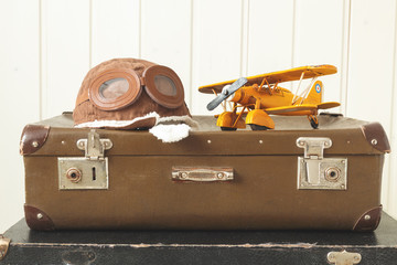 Helmet pilot and toy yellow metal plane Two old retro suitcases White wooden background Vintage tinting