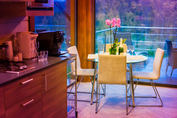 View of the served table against the background of panoramic windows. Glass laid table. Orchids on the table. Hi tech furniture.