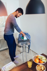 Attractive american black man is ironing shirt at home.