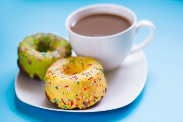 Two colored donuts on a plate with a cup of coffee. Yellow and Green Donut on a blue background. Dessert