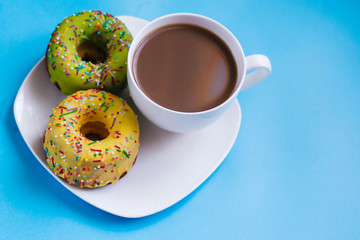 Two colored donuts on a plate with a cup of coffee. Yellow and Green Donut on a blue background. Dessert
