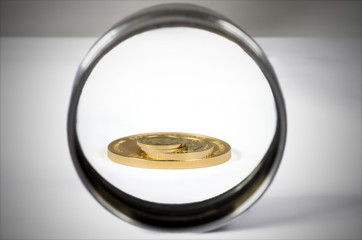 A pile of gold coins of various sizes is visible in a magnifying glass.