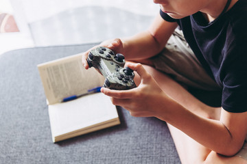 Blond child playing video games instead of studying sitting home sofa with legs crossed young student resting playing online with friends domestic pastime challenge web Close up hands no face