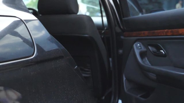 Hand of male businessman opens and holds door of car for beautiful young woman. Man opening door of automobile for female passenger. Businesswoman get into the auto. Close up Slow motion
