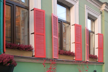 Image of three windows with red shutters and flowers on the windowsills