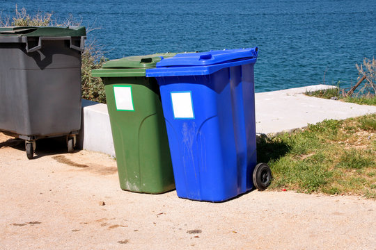 Trash can, garbage bin, recycling bin in tourist complex by sea, side of road waiting to be picked up by garbage truck. Blue and green containers for waste sorting, sort garbage for paper and glass.
