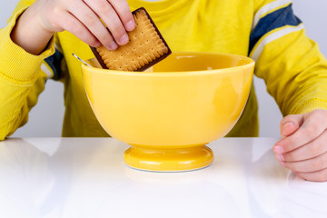 child dipping his chocolate biscuit in his bowl of milk