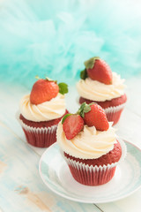 Three cupcake red velvet with a cap of cream cheese and strawberries on a blue background