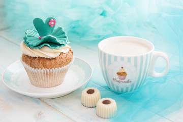 Cupcake and a mug on turquoise background. Bright blue wooden table