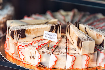 Closeup of chocolate coconut cream cheese cheesecakes swirl slices dessert on tray window display in gourmet bakery Italian cafe with sign