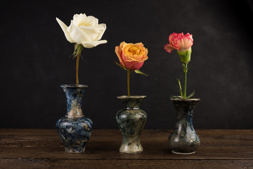 Three small marble vases with roses on black background