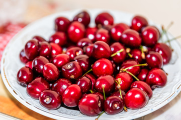 Macro closeup of red bright vibrant washed cherries on white plate in home table during summer season with stems