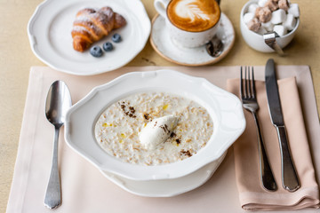 Bowl of breakfast oatmeal with soft Italian cheese and cinnamon. Croissants, coffee and other dishes on the table in the restaurant
