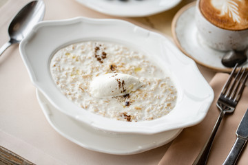 Bowl of breakfast oatmeal with soft Italian cheese and cinnamon. Croissants, coffee and other dishes on the table in the restaurant