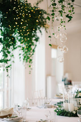 Little balls with candles hang from floral garland over wedding dinner table