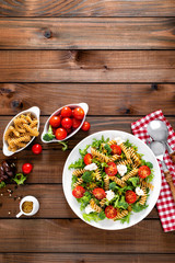 Italian pasta salad with wholegrain fusilli, fresh tomato, cheese, lettuce and broccoli on wooden rustic background. Mediterranean cuisine. Cooking lunch. Healthy diet food. Top view