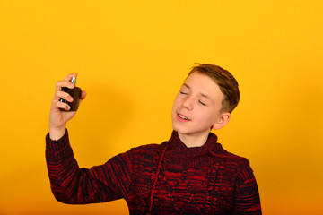 The boy uses perfume and sprinkles cologne on himself in the studio on a yellow background.