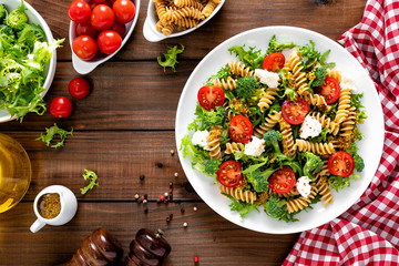 Italian pasta salad with wholegrain fusilli, fresh tomato, cheese, lettuce and broccoli on wooden...