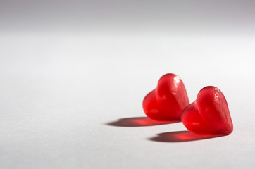 Fototapeta premium illuminated small hearts with shadows on white background; heart-shaped jelly candy like pieces of glass