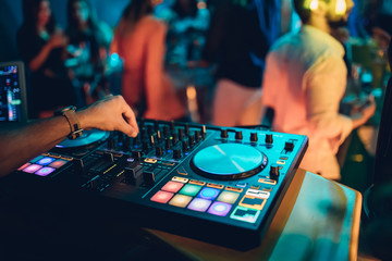 Fototapeta premium DJ plays live set and mixing music on turntable console at stage in the night club. Disc Jokey Hands on a sound mixer station at club party. DJ mixer controller panel for playing music and partying.
