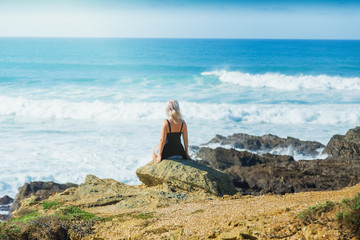 Girl sitting on the rocks and looks at ocean