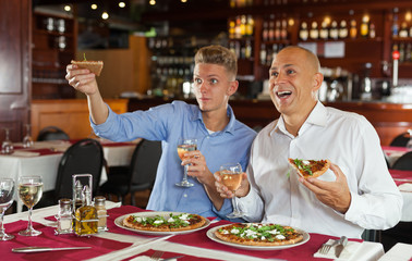 Male friends watching sport match and enjoying pizza in restaurant