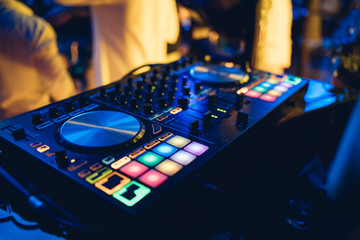 Naklejka premium DJ plays live set and mixing music on turntable console at stage in the night club. Disc Jokey Hands on a sound mixer station at club party. DJ mixer controller panel for playing music and partying.