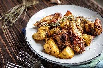Baked chicken wings with potatoes and garlic on a rustic background