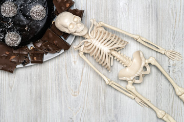 Chocolate cake and slices on a plate and skeleton on a wooden table. Flat lay. Concept of death from diabetes.