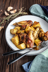 Baked chicken wings with potatoes and garlic on a rustic background