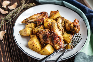 Baked chicken wings with potatoes and garlic on a rustic background