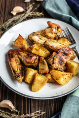 Baked chicken wings with potatoes and garlic on a rustic background