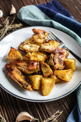 Baked chicken wings with potatoes and garlic on a rustic background
