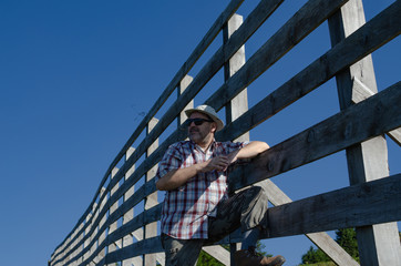 Farmer leaned on a wooden fence with clear blue sky above him