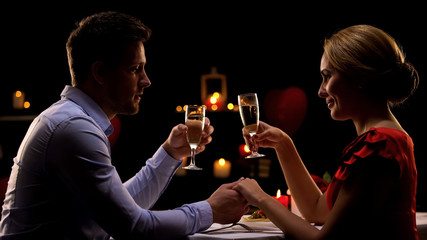 Adorable couple holding hands and drinking champagne during romantic date