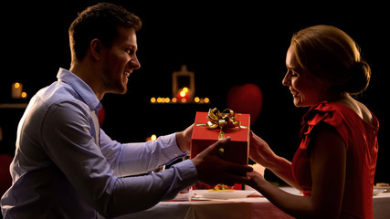 Man presenting lady red gift box, Valentines day surprise, romantic dinner