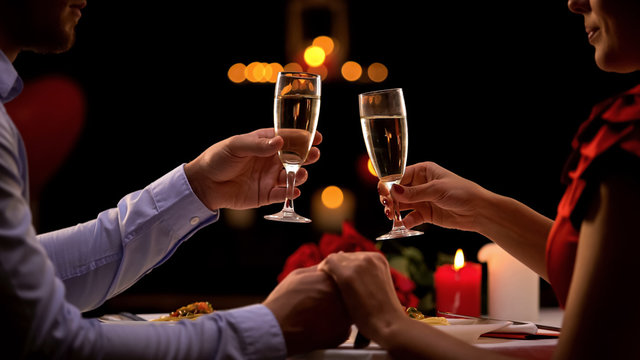 Nice couple holding hands, drinking champagne during romantic date, anniversary