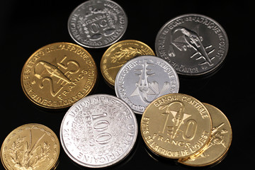 A macro image of an assortment of West African Franc coins on a reflective black background