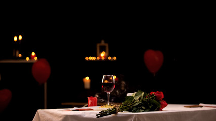Red roses on table near glass of wine, romantic atmosphere, st Valentines Day