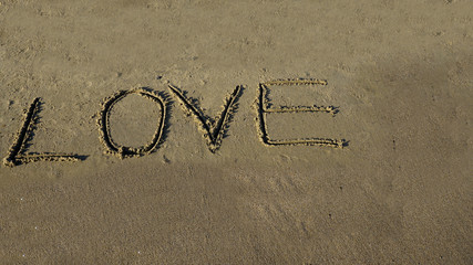 Love word written in sand on wet sandy beach. New summer is coming, holiday vacation travel day time concept. I love summer and need holiday message on coast. Copy space for ad banner.