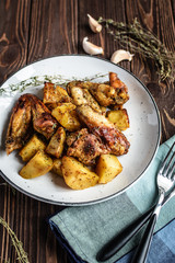 Baked chicken wings with potatoes and garlic on a rustic background