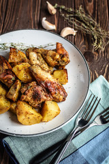 Baked chicken wings with potatoes and garlic on a rustic background