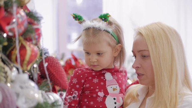 A woman holding a little daughter in her arms at a decorated Christmas tree.
