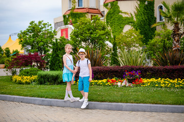 Obraz premium Blonde girl in white and blue dress and ginger boy in the hat and big glasses in the summer park with decorations